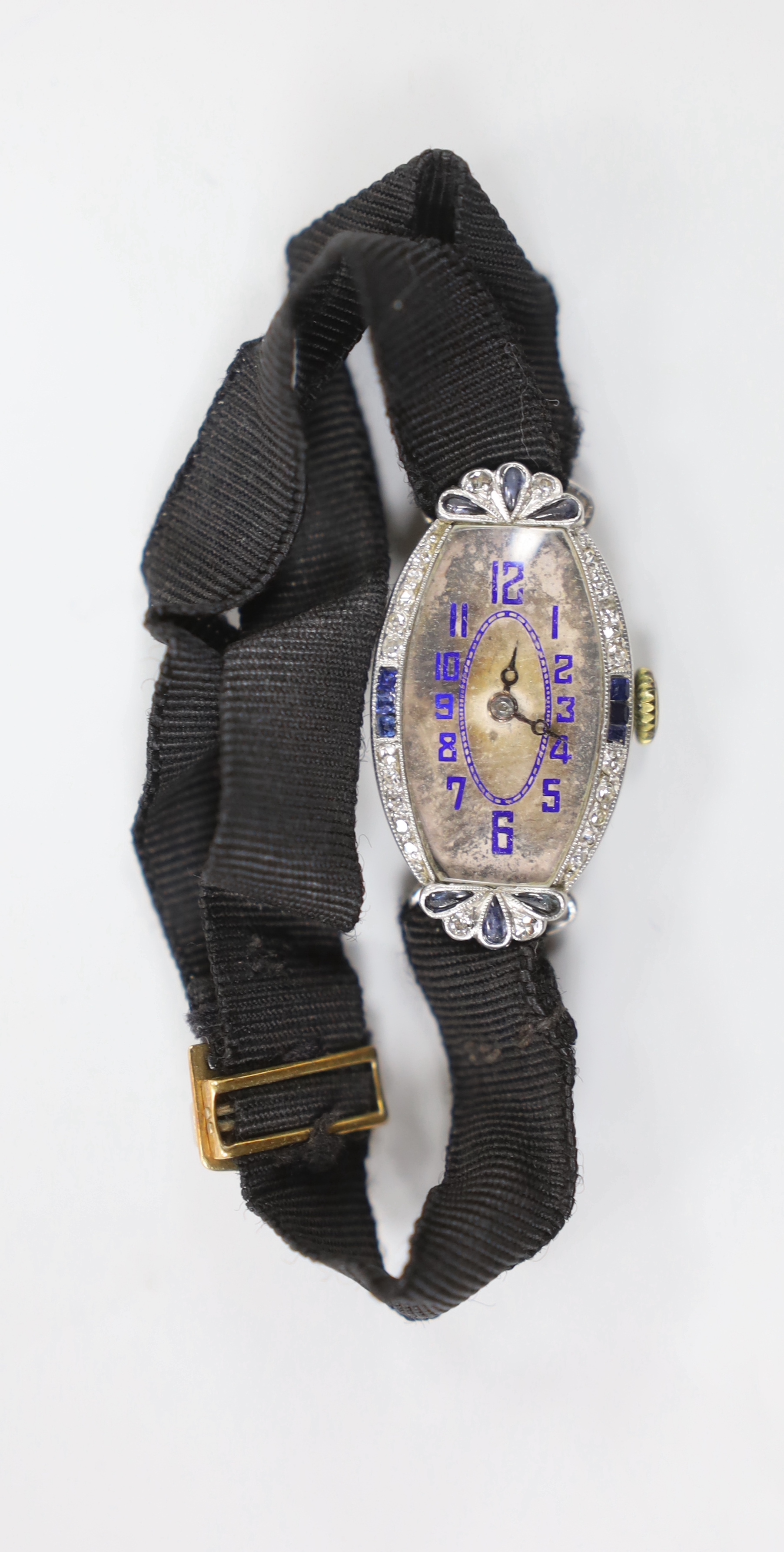A lady's 1920's/1930's white metal, sapphire and diamond chip set tonneau shaped cocktail watch, on a fabric strap, with sapphire and diamond chip set buckle.